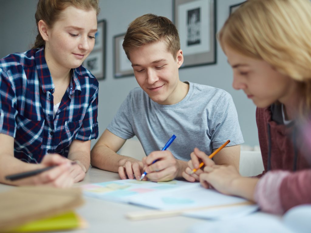 Trīš studenti pie galda raksta projektu